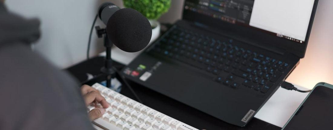 A person at a desk with a laptop, microphone, and keyboard in a modern setup.
