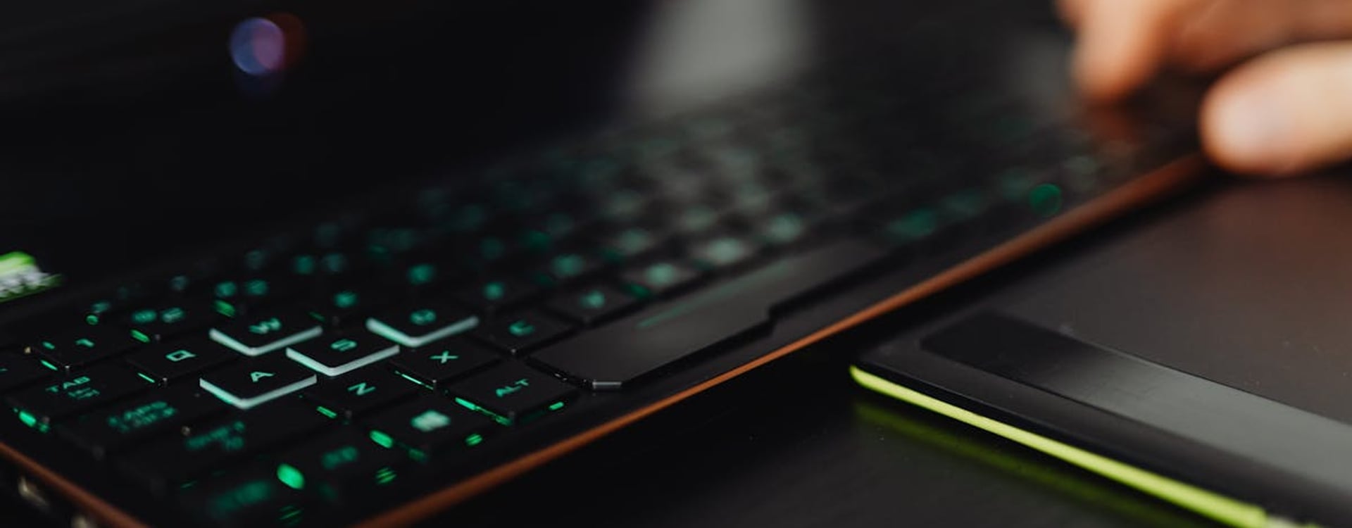 A close-up of a backlit gaming keyboard and laptop, highlighting modern technology use.