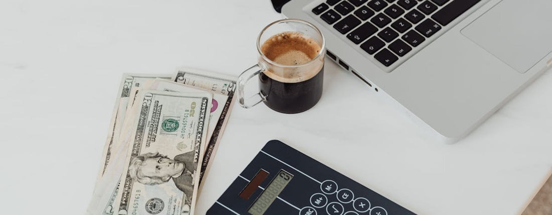 A modern workspace featuring a calculator, cash, and laptop with coffee.