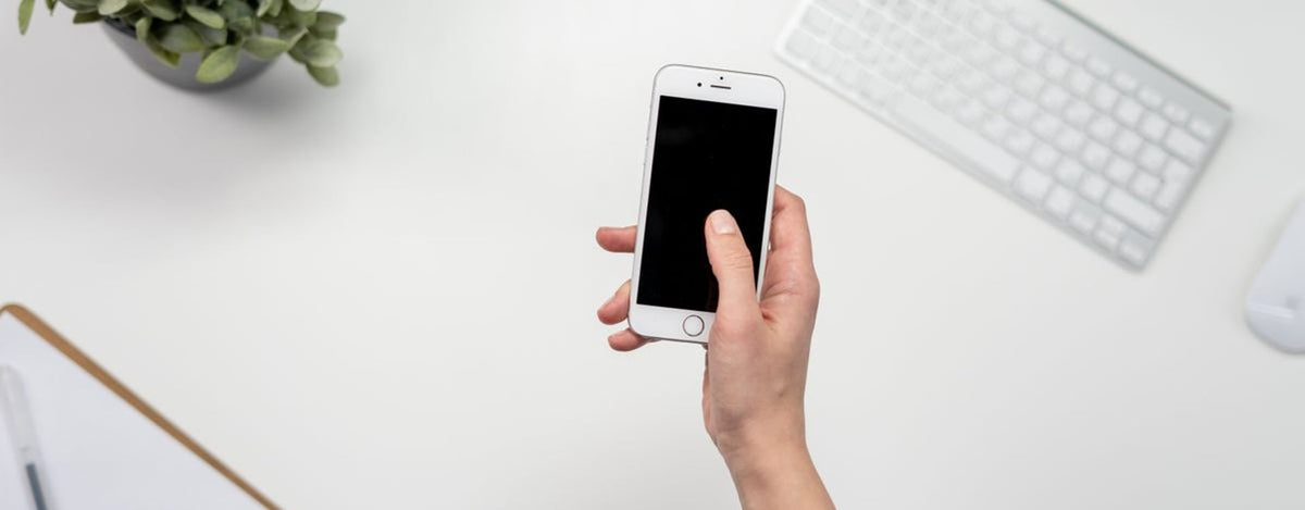 Top view of a minimalist workspace featuring a smartphone, keyboard, and plant.