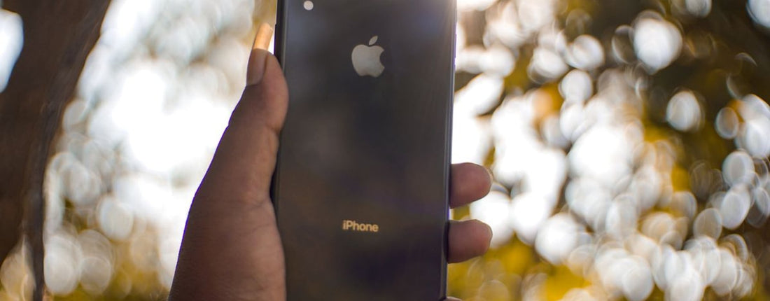 A hand holding a smartphone outdoors with bokeh effect in the background.