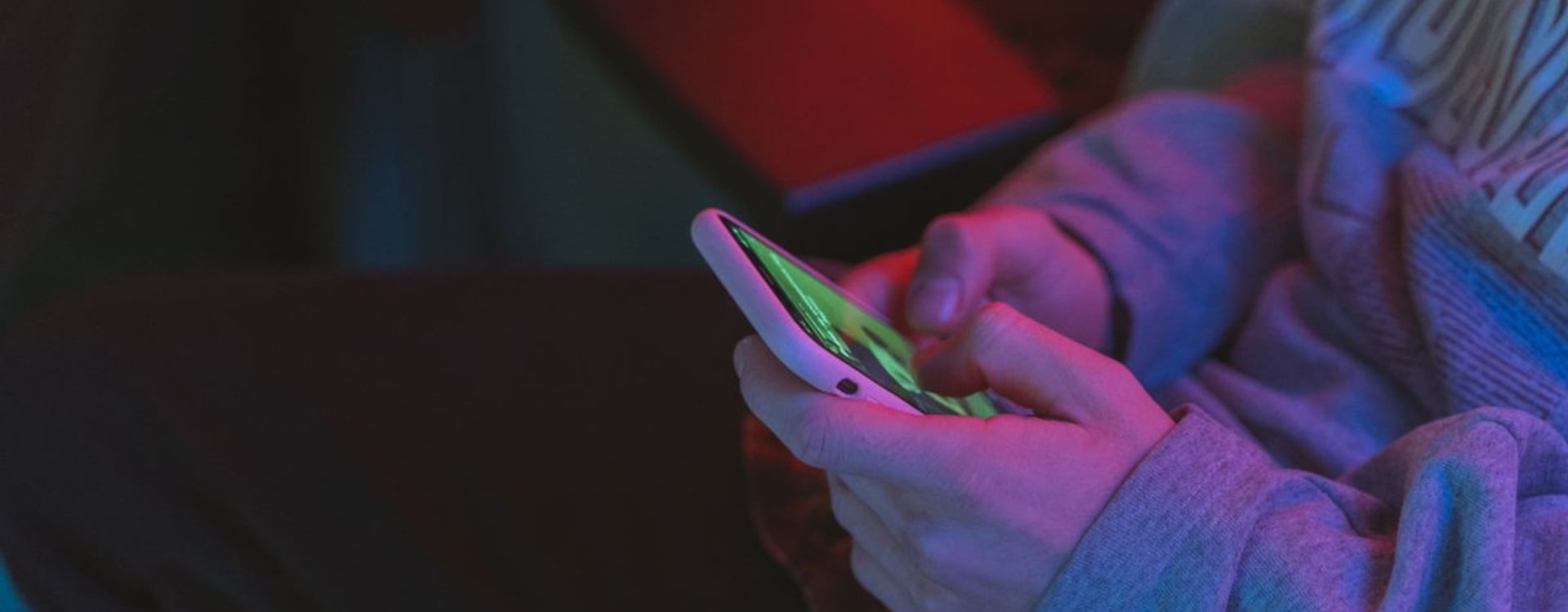 Close-up of hands holding a smartphone in a dimly lit indoor setting with neon lighting.