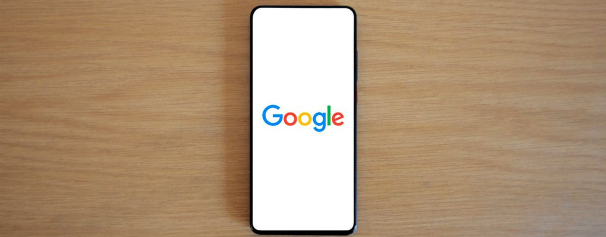 A smartphone displaying the Google homepage on a wooden surface, viewed from above.
