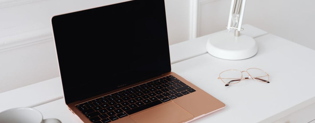 A modern sleek workspace featuring a laptop, desk lamp, and glasses on a white table.