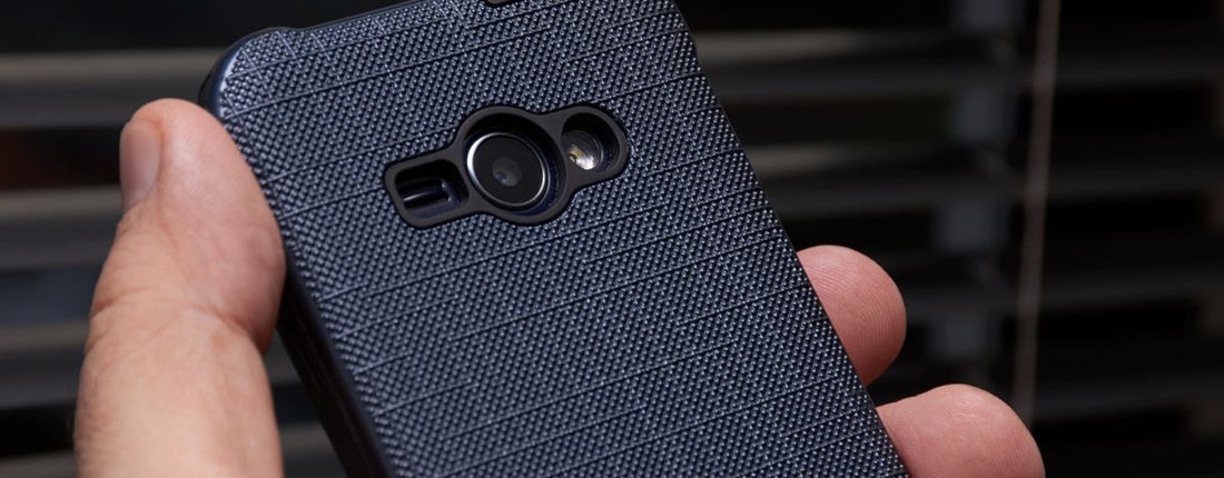 A close-up of a hand holding a smartphone with a textured blue case near a window, showcasing modern technology.