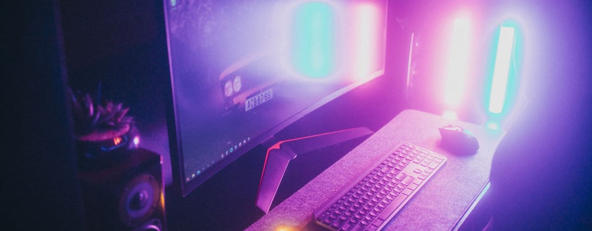 A stylish gaming desk featuring neon lights, keyboard, and monitor in a dark room.