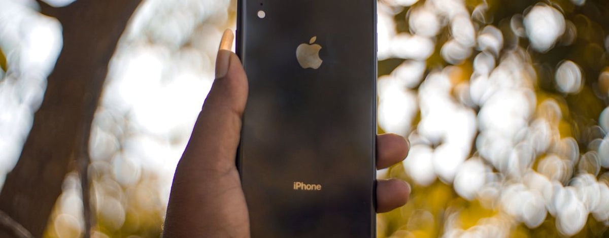 Close-up of a hand holding a smartphone outdoors with blurred background of trees.